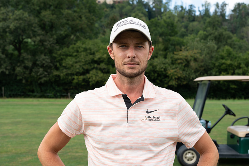 Portrait Steffen Wahl im Golfoutfit vor einer grünen Wiese und einem Golfcart