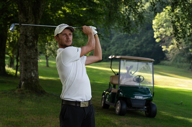 Der Golftrainer Steffen Wahl steht vor einem Golfcar und blickt konzentriert seinem gerade geschlagenen Golfball hinterher